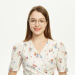 Young woman wearing glasses smiling in a floral outfit against a plain background.